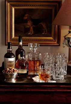 an assortment of liquors and glasses on a table in front of a framed painting