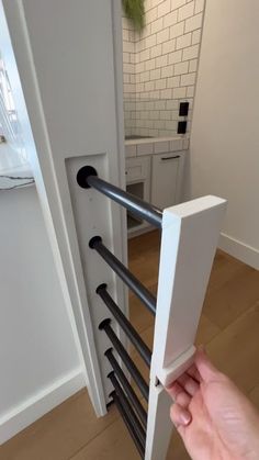 a hand is holding the door handle to an open white cabinet with black bars on it