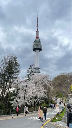 people walking on the street in front of a tall building with a tv tower behind it