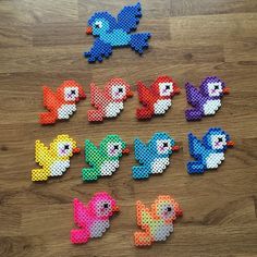 several different colored birds made out of perler beads on a wooden floor with one bird in the middle