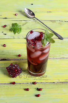 a glass filled with ice and garnish on top of a wooden table next to a spoon