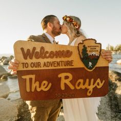 a bride and groom kissing while holding a welcome sign