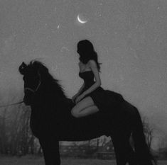 a woman sitting on the back of a horse next to a full moon in black and white