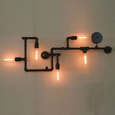 three pipes are connected to the wall with light bulbs on each side and a clock in between them