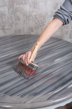 a person holding a brush on top of a metal table in front of a wall