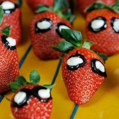 strawberries with googly eyes and green leaves on yellow tableclothed surface, closeup