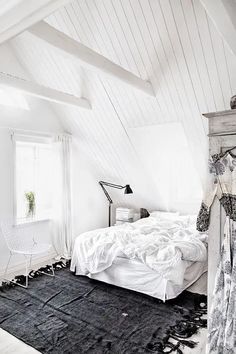 an attic bedroom with white walls and black rugs on the floor, along with a large bed