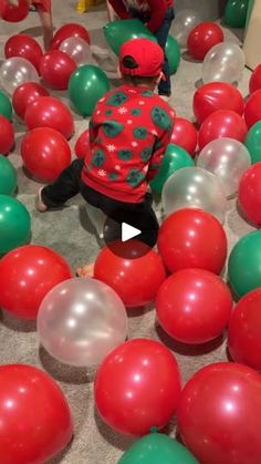 a toddler playing with red and green balloons in a room filled with other children