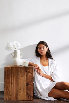 a woman sitting on the floor next to a table with a vase and flowers in it