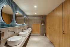 a bathroom with two sinks and three mirrors on the wall, along with wooden cabinets