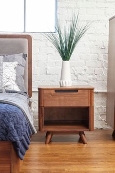 a nightstand with a plant in it next to a bed