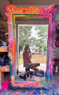 a woman sitting on the ground in front of a mirror with paint all over it