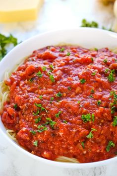 a white bowl filled with pasta covered in marinara sauce and parsley on the side