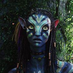 a woman with blue face paint and long braids standing in front of some trees