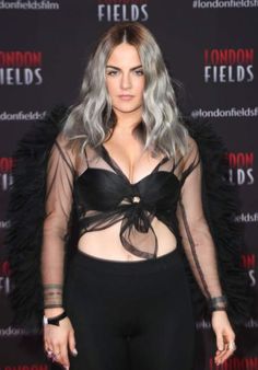 a woman with blonde hair and black outfit posing for the camera in front of a london fields backdrop