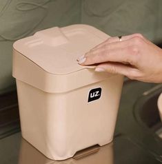 a woman's hand is on the lid of a beige storage container that sits on top of a glass table