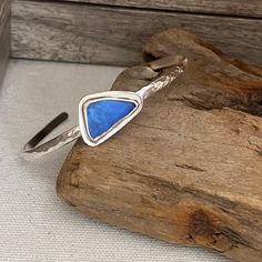 a silver ring with a blue triangle on it sitting on top of a piece of wood