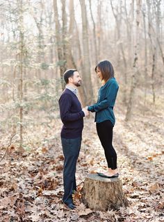 a man and woman standing on top of a tree stump in the middle of a forest