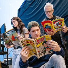 an older man reading a comic book with two younger people watching him from the side