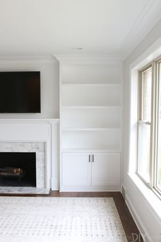 an empty living room with white bookcases and a fireplace