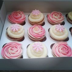 twelve cupcakes with pink and white frosting in a box