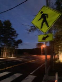 there is a pedestrian crossing sign on the side of the road at night with trees in the background