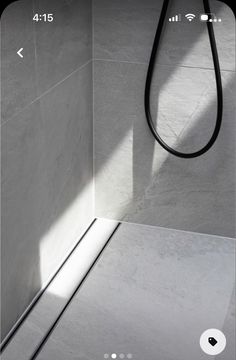 a shower head in the corner of a white tiled bathroom with a black hose hanging from it's side