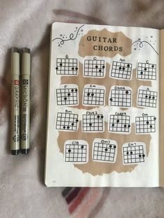 an open notebook with guitar chords on it next to two markers and one pen,