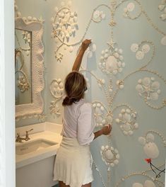 a woman painting a wall with pearls on it in a room that has a sink and mirror