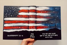 a hand holding an open bible with the american flag painted on it and words below