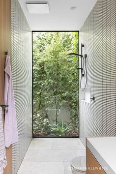 a bathroom with a glass door leading into the shower area and outside trees in the background