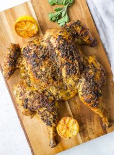 a whole chicken on a cutting board with lemons and herbs