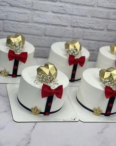 four small white cakes with red bows and gold decorations on each cake, sitting on a table