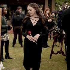 a woman in a black dress standing next to a mirror and holding a red rose