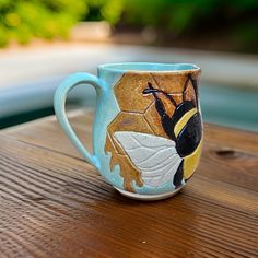 a coffee cup with a bee painted on it sitting on top of a wooden table