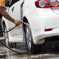 a man is washing his white car with a high pressure washer and water hose