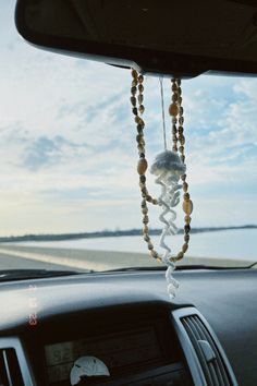 a car dashboard with beads hanging from it's dash board and an ocean in the background