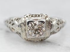 This Art Deco diamond engagement ring features exquisite detail! Made of 18-karat white gold, this ring is a square variety of the filigree basket settings of the 1920’s. The main focus is the large diamond adorning the center, flush-set so that the diamond sits perfectly flat inside the setting. The pierced, engraved floral images on the shoulders are detailed and lovely!Metal: 18K White GoldGem: Diamond .44 Carats, SI2 in Clarity, L in ColorGem Measurements: 4.9 mm, RoundRing Size: 7Marks: "18K" Stamped on the inside Round Cut Diamond Ring, Engagement Ring Round Cut, Art Deco Diamond Ring Engagement, European Cut Diamond Ring, Engagement Ring Round, Filigree Engagement Ring, White Gold Diamond Engagement Ring, Handmade Engagement Rings, Round Cut Engagement Rings