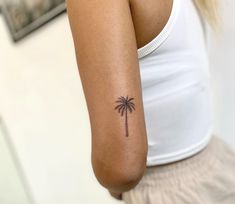 a woman's arm with a small palm tree tattoo on the left side of her arm