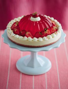 a cake with strawberries on top is sitting on a blue plate and red tablecloth