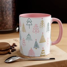 a pink and white coffee mug sitting on top of a wooden table next to a cookie