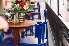 two vases with flowers sit on top of a wooden table next to blue chairs