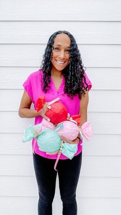 a woman standing in front of a white wall holding two heart shaped balloons with ribbons on them