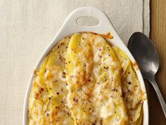 a casserole dish with potatoes and cheese in it on a white plate next to a spoon