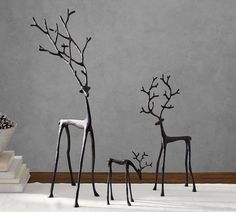 three metal deer sculptures sitting on top of a white floor next to a book shelf