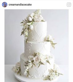 a three tiered white wedding cake with flowers on it's sides and leaves