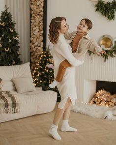 a woman holding a small child in her arms while standing on the floor next to a christmas tree