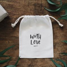 a white bag with the words with love printed on it next to some green leaves