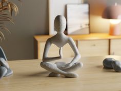 a statue of a person sitting in a yoga position on a table next to some rocks