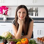 a woman sitting in front of a table full of fruits and vegetables, smiling at the camera